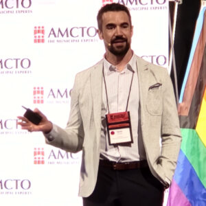 Man on a stage speaks out toward a live audience.